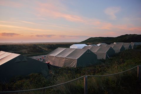 Zelte in Dünenlandschaft bei Sonnenuntergang mit Meer im Hintergrund