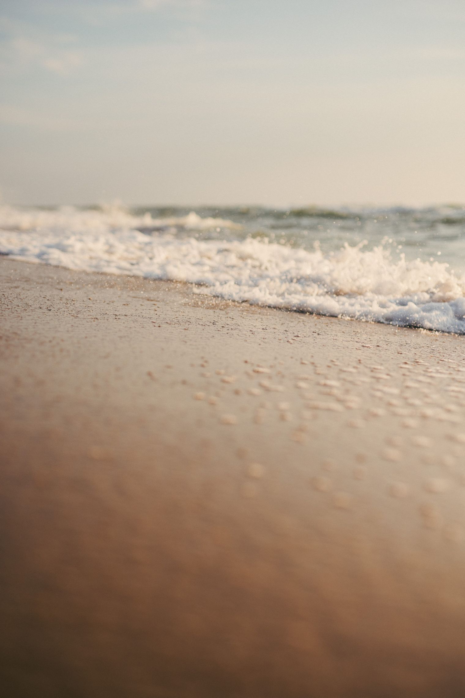 Nahaufnahme einer Meereswelle, die an den sandigen Strand schwappt.