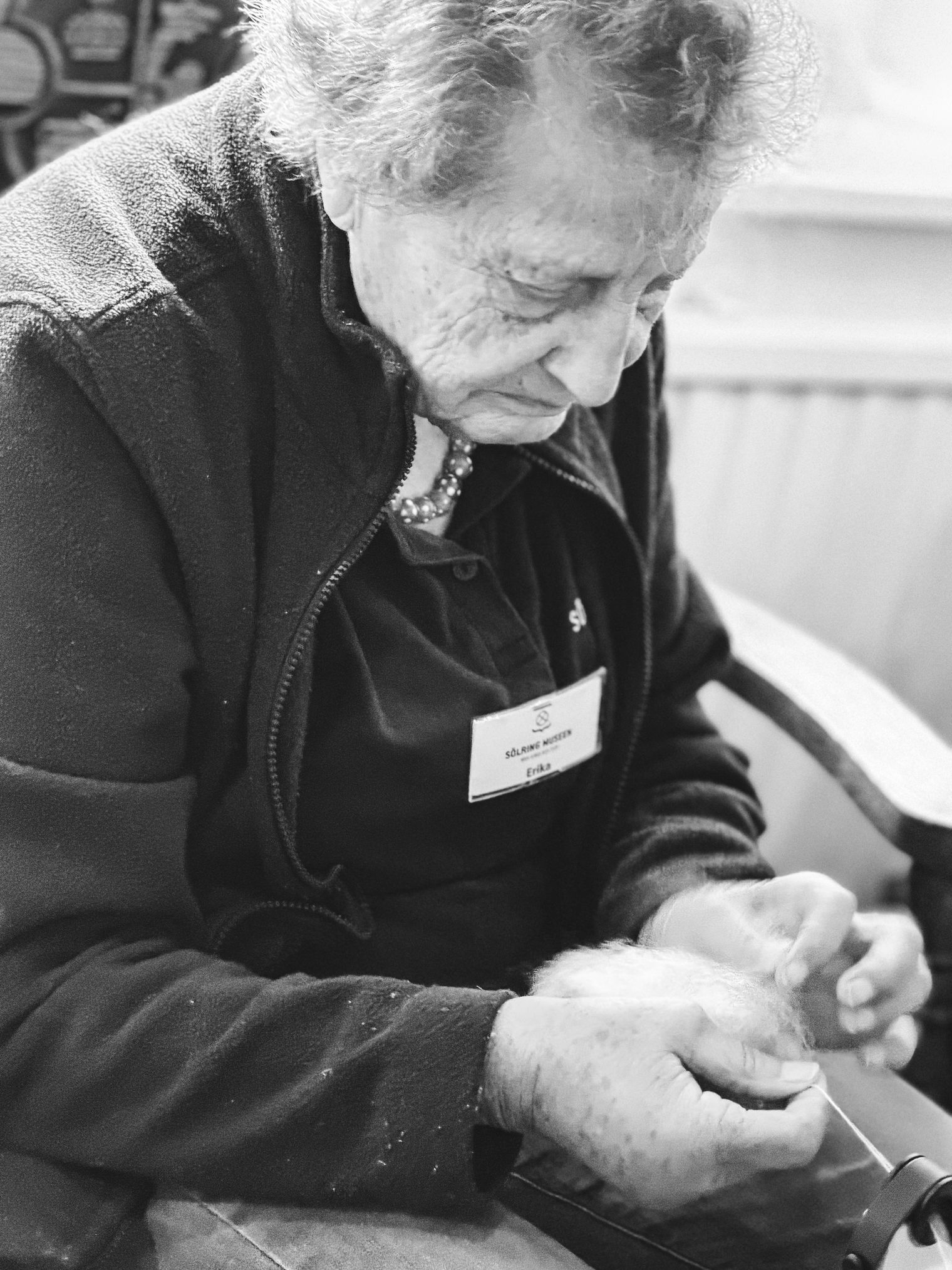 Ältere Frau hält Wollfasern und spinnt sorgfältig. 