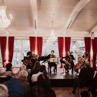 Streichensemble spielt Kammermusik vor Publikum in elegantem Saal.