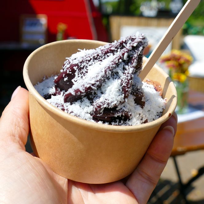 Becher mit dunklem Eis und Kokosflocken in Hand gehalten