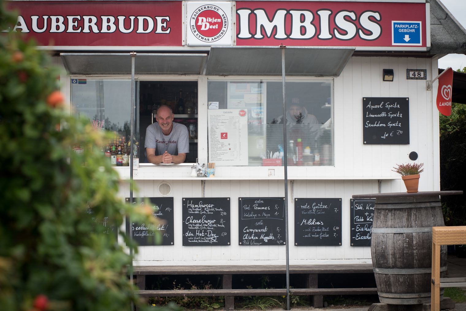 Lächelnder Imbissverkäufer am Fenster der Zauberbude mit Speisetafeln.