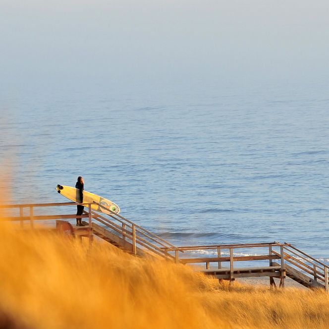 Ein Surfer mit Board steht am Strandübergang in Westerland und blickt aufs Meer.