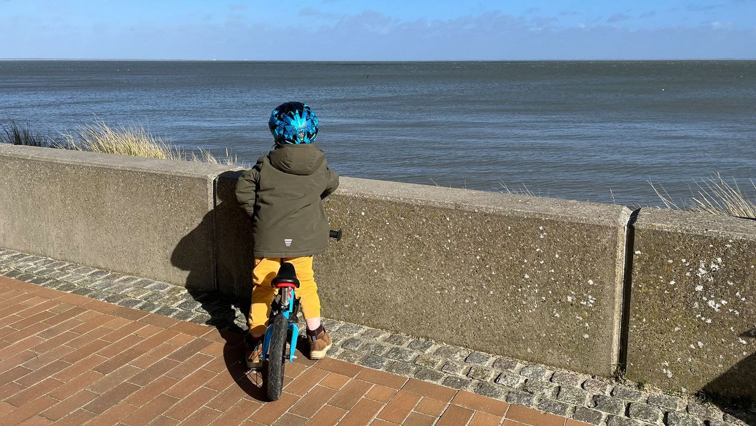 Kind mit Laufrad blickt von der Lister Promenade aufs Meer.