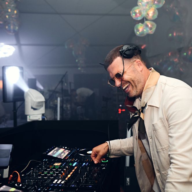 Ein lachender Mann mit Kopfhörern am DJ-Pult