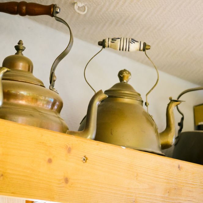 Mehrere alte Metallteekessel stehen auf einem Holzregal. 