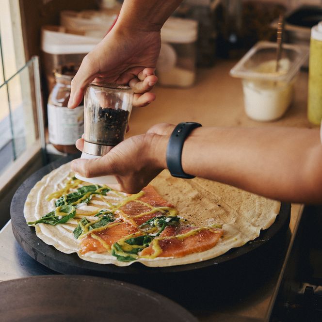 Person würzt Crêpe mit Lachs und Kräutern auf heißer Platte. 