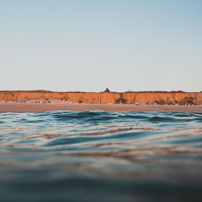 Blick vom Wasser auf das Rote Kliff in Kampen mit Strandkörben am Strand.