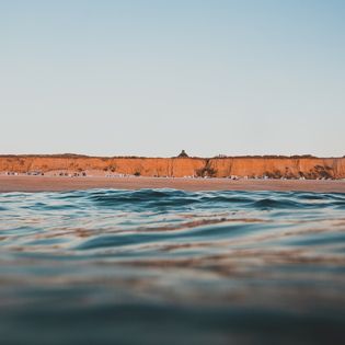 Blick vom Wasser auf das Rote Kliff in Kampen mit Strandkörben am Strand.