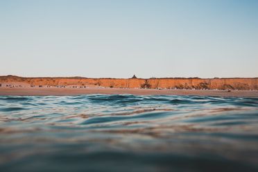 Blick vom Wasser auf das Rote Kliff in Kampen mit Strandkörben am Strand.