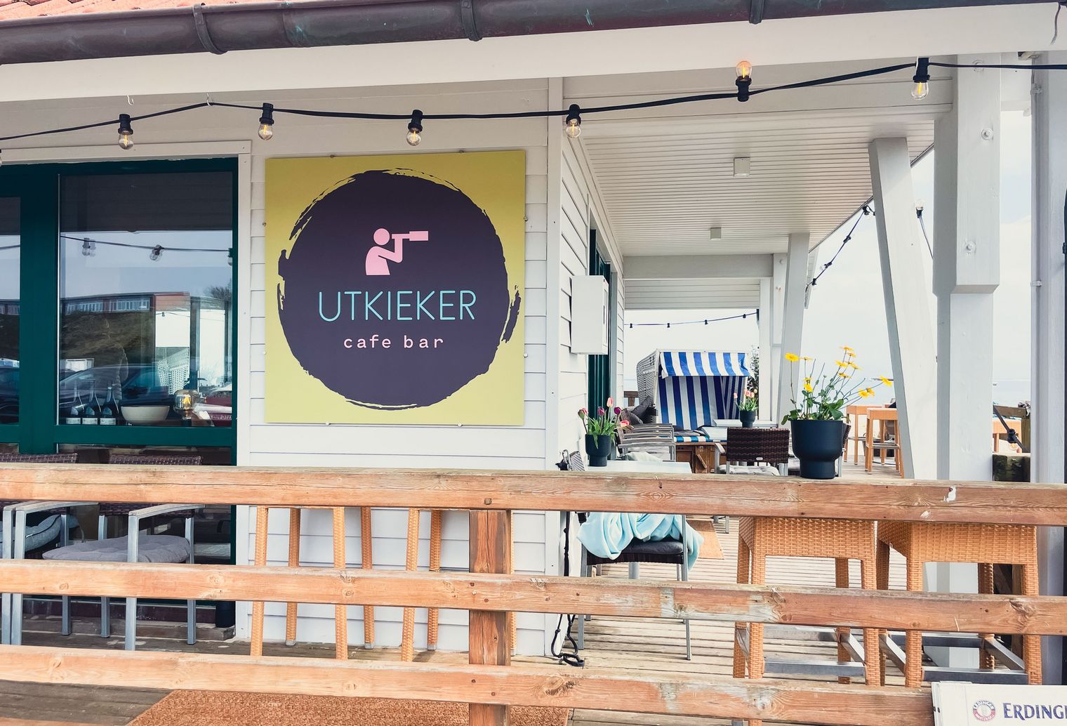 Holzveranda mit Schild „UTKIEKER cafe bar“ und Sitzbereich