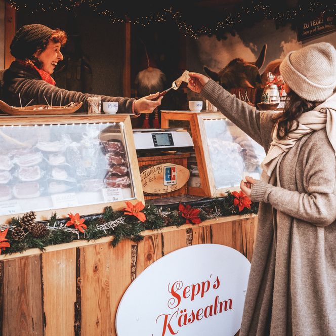 Frau erhält Käseprobe an festlich geschmücktem Stand auf dem Sylter Wintermarkt.
