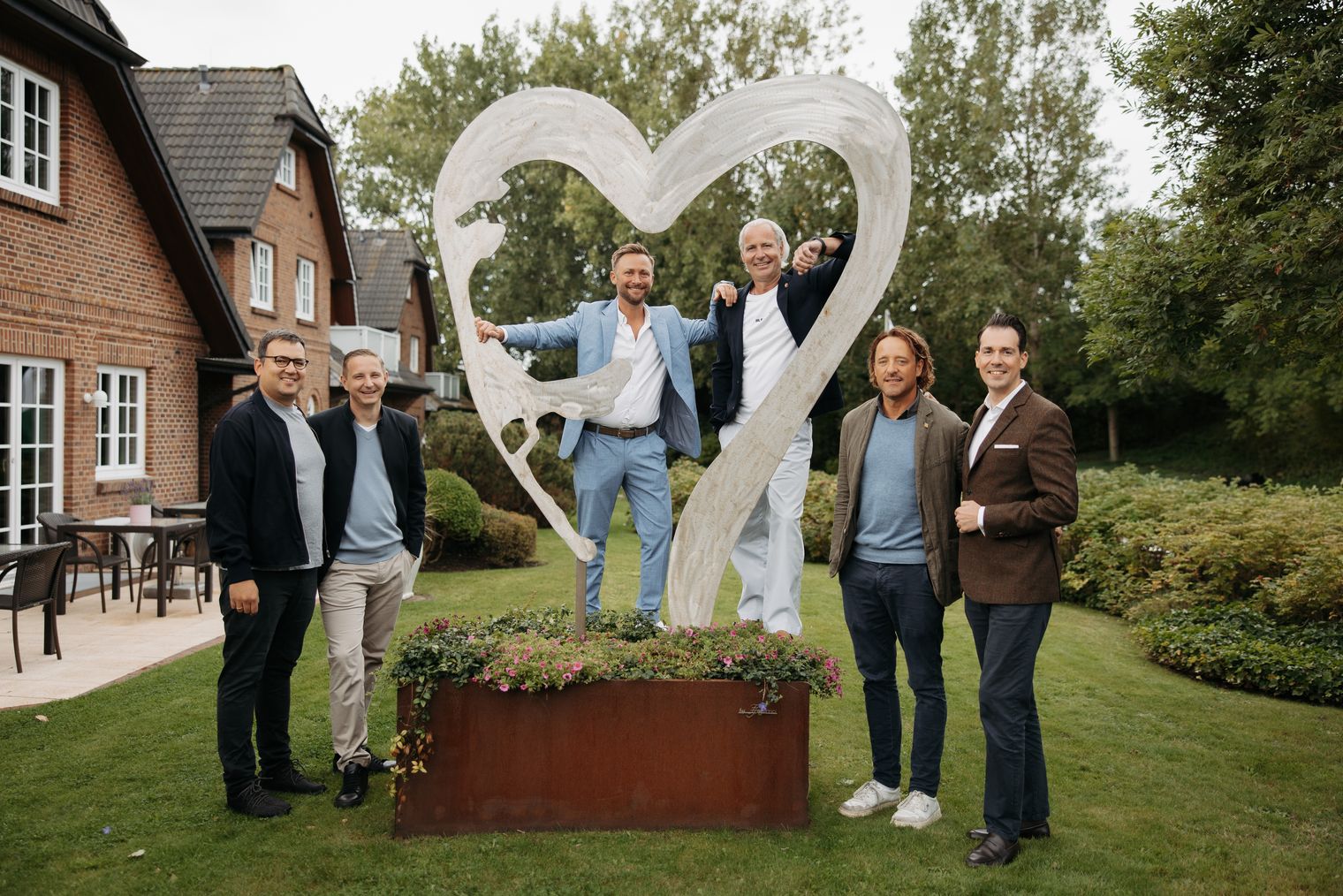Sechs Männer stehen im Garten vor einer Skulptur mit Insel-Silhouette.
