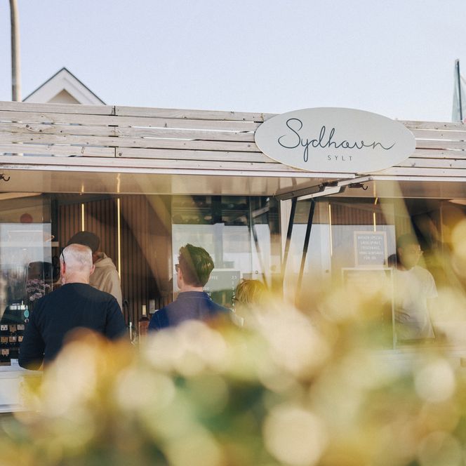 Menschen bestellen bei sonnigem Wetter am Imbisscontainer „Sydhavn Sylt“
