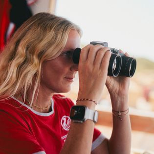 Rettungsschwimmerin mit Fernglas schaut aufmerksam zum Strand.