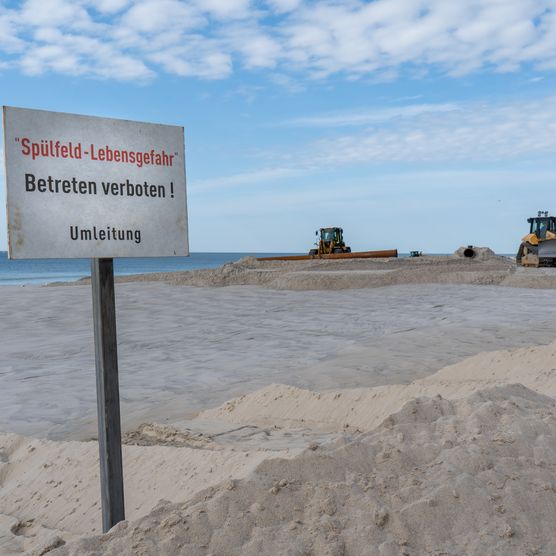Schild am Strand weist auf die Sandvorspülung hin
