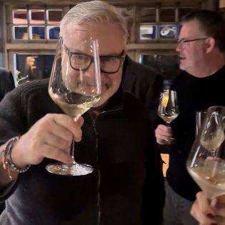 Mann mit Brille hebt ein Weinglas mit Weißwein