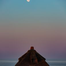 Reetdachhaus auf Sylt bei Dämmerung mit Mond über dem Meer.
