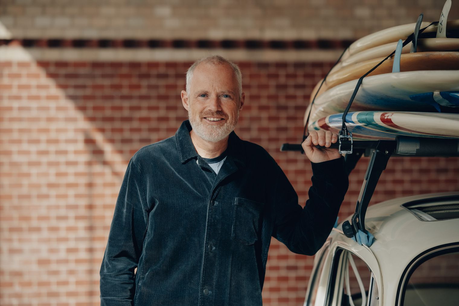 Moritz Luft von Sylt Marketing steht neben einem Auto mit auf dem Dach befestigten Surfbrettern.