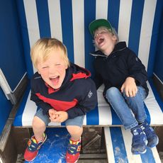 Zwei lachende Jungen sitzen in einem blau-weißen Strandkorb.
