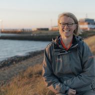 Lächelnde Frau in Outdoorjacke sitzt an der Küste von Sylt