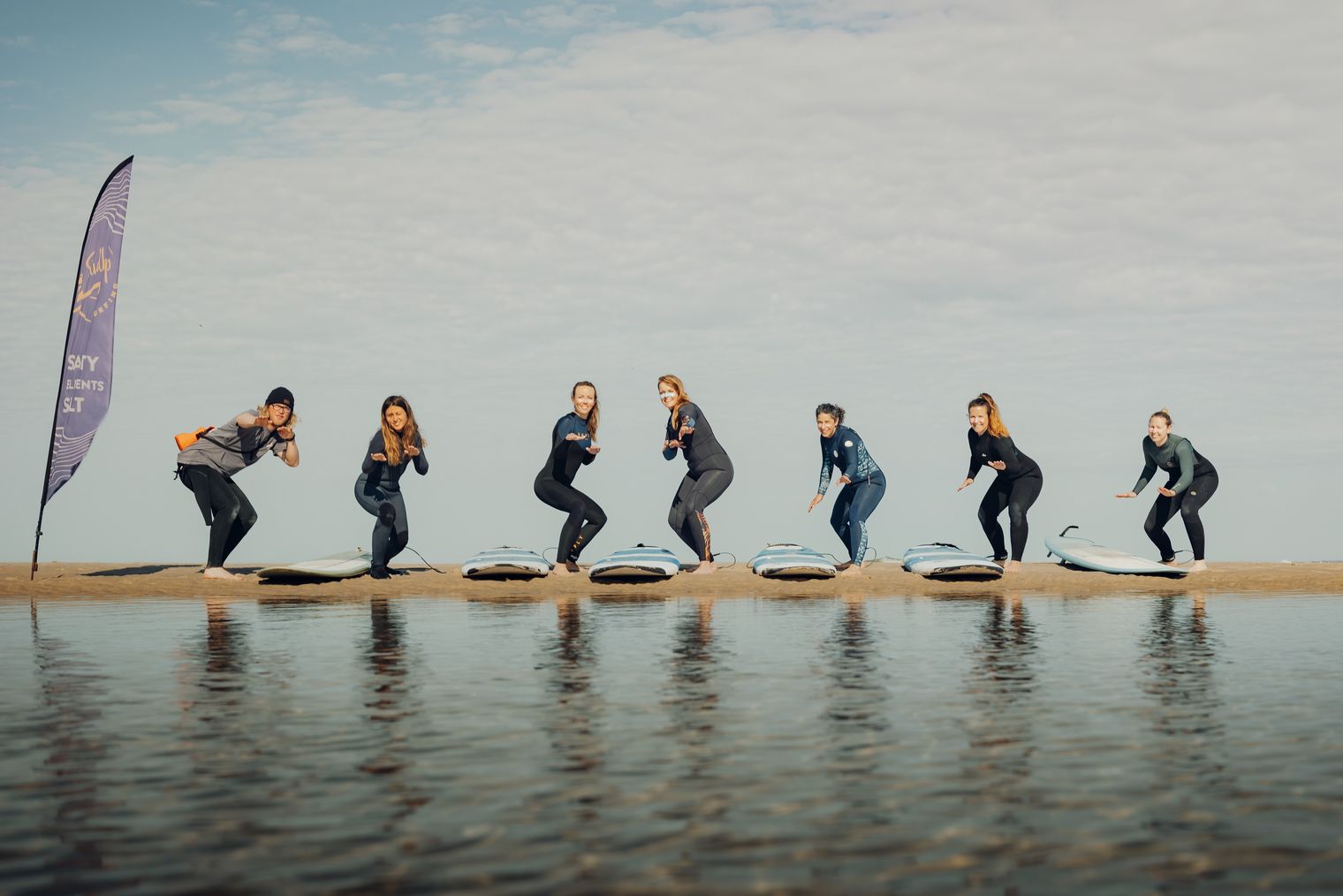 Sieben Frauen üben das Stehen auf dem Surfbrett am Strand