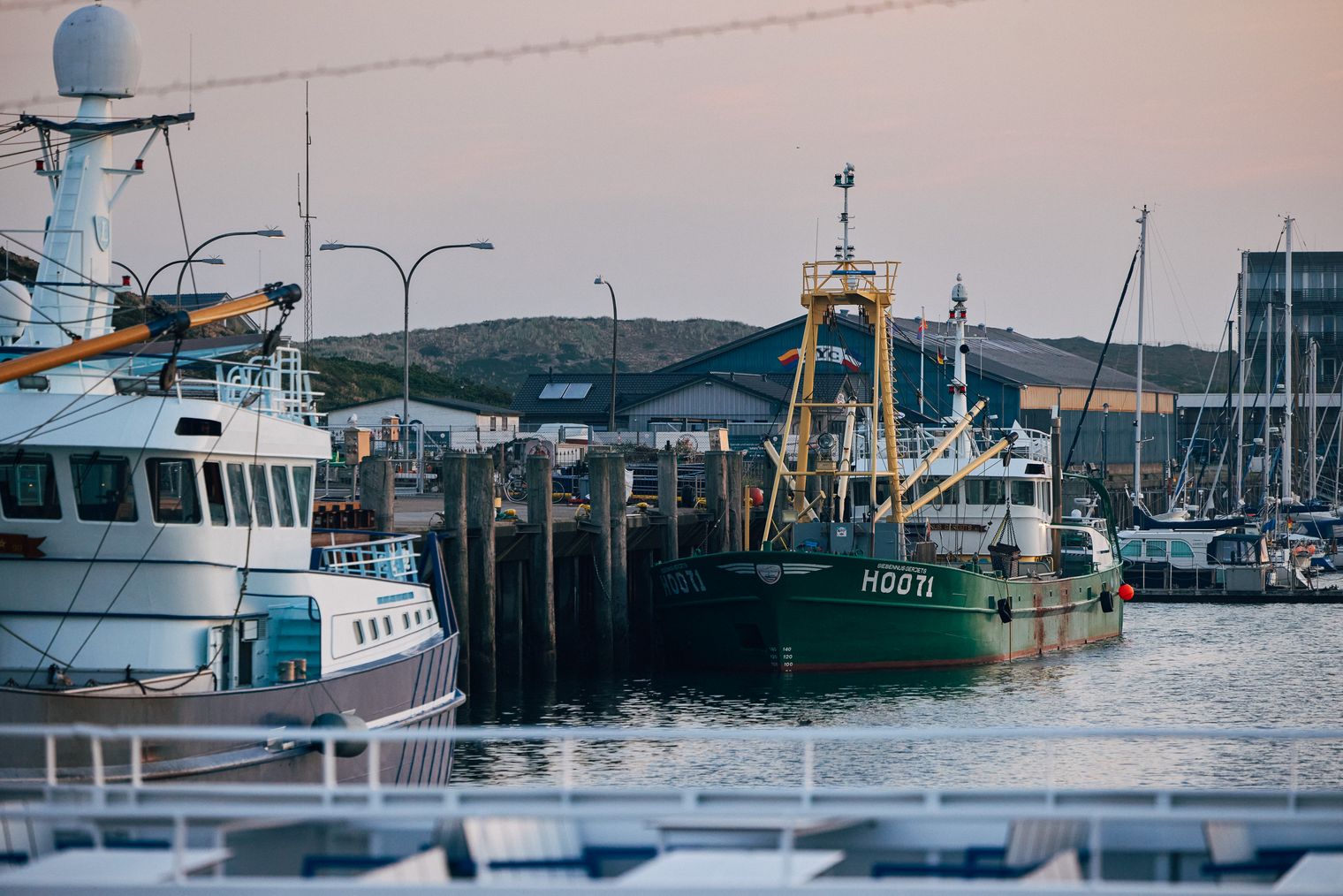 Fischerboote und Hafenanlagen bei Sonnenuntergang, grünes Boot mit der Aufschrift "H0071" im Vordergrund.