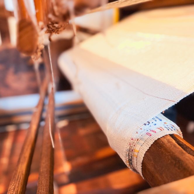 Nahaufnahme von hellem Stoff, der am Webstuhl entsteht. 