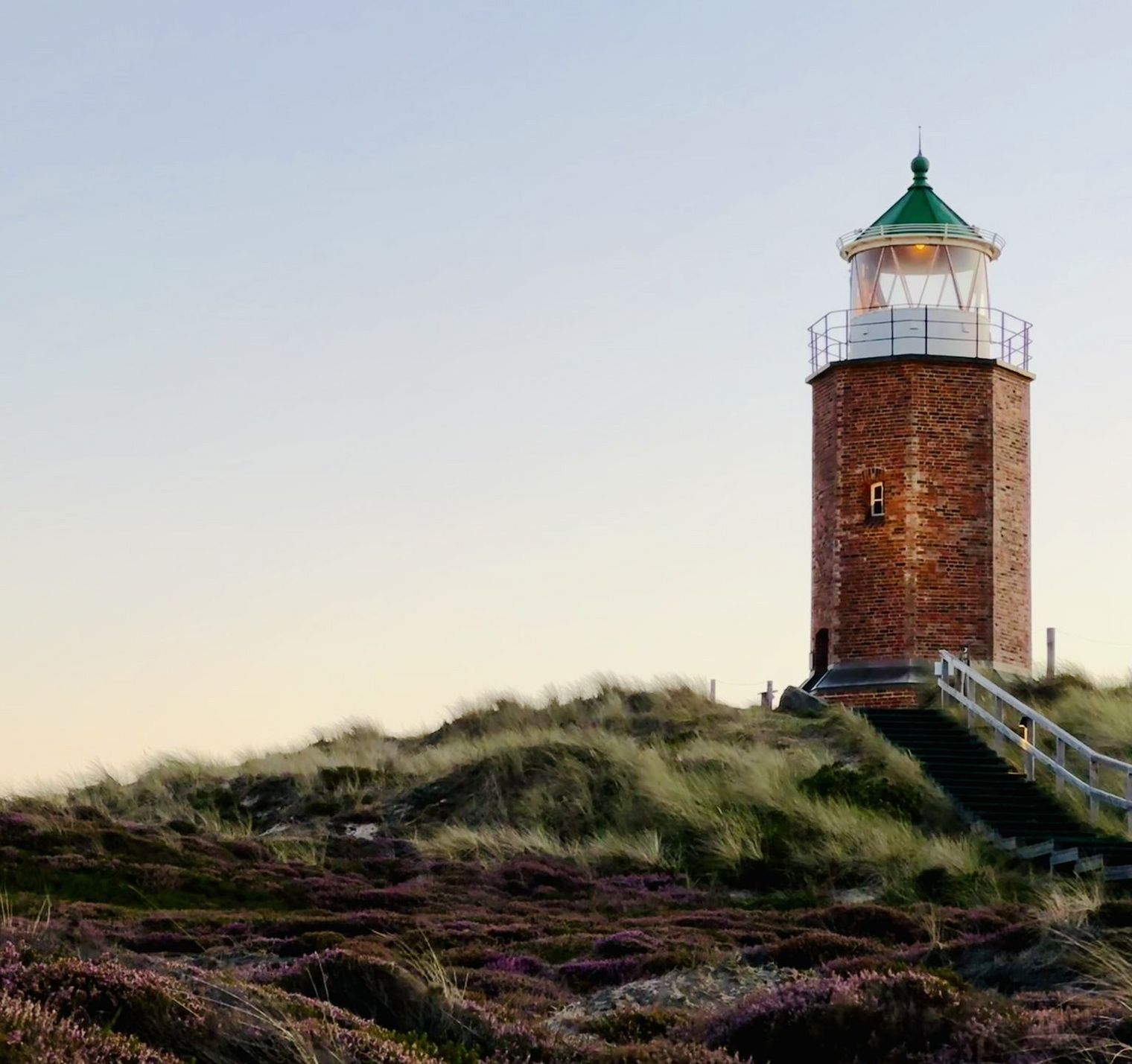 Backsteinleuchtturm bei Sonnenuntergang in blühender Heide.