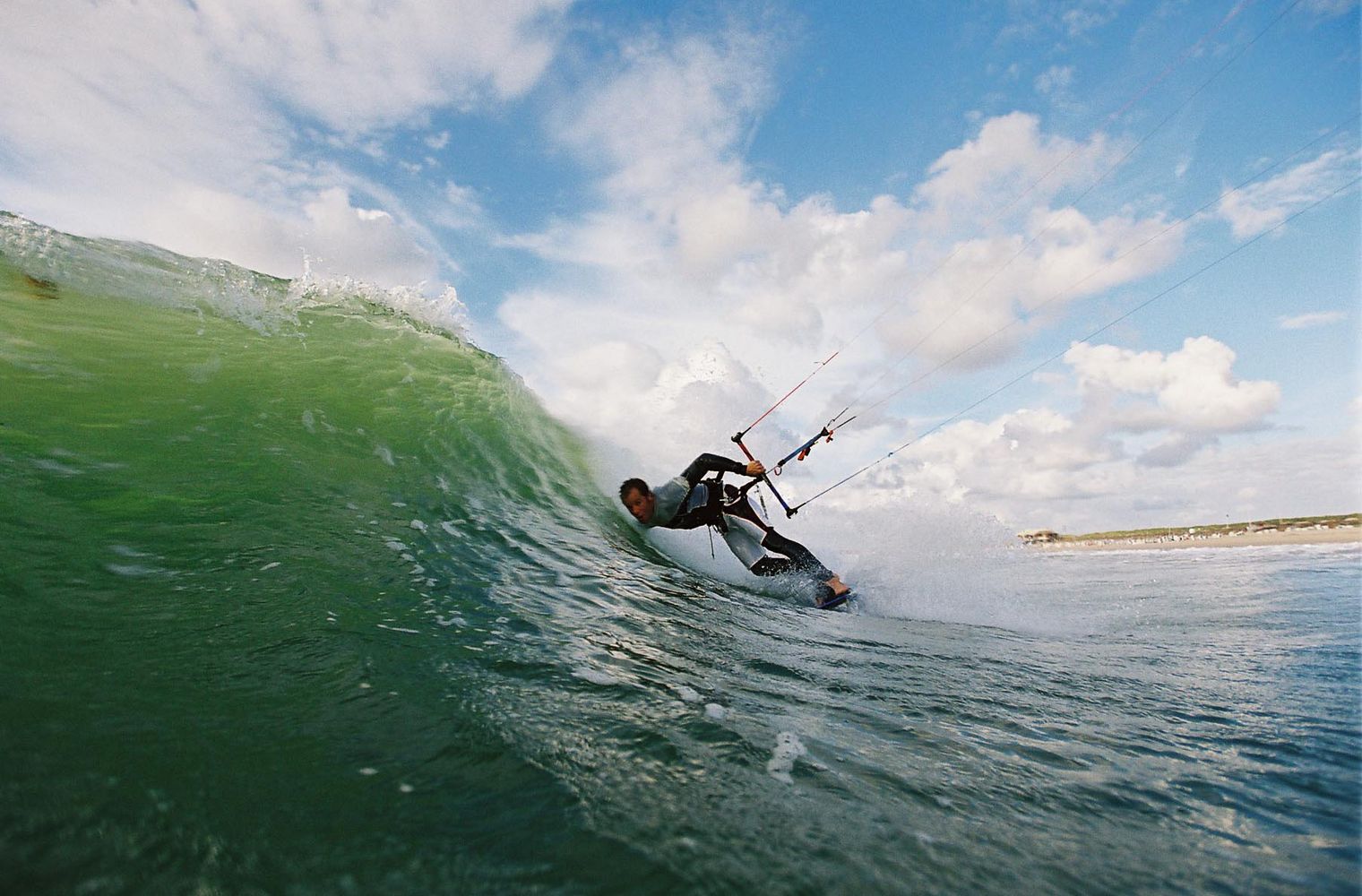 Kitesurfer fährt in gebückter Haltung durch eine grüne Welle