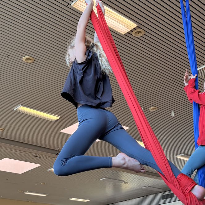 Kind macht Akrobatik am roten Vertikaltuch