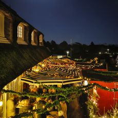 Weihnachtsmarkt in Kampen bei Nacht, beleuchtet von Lichterketten und einem strahlenden Vollmond, mit geschmückten Marktständen und Reetdachhäusern.