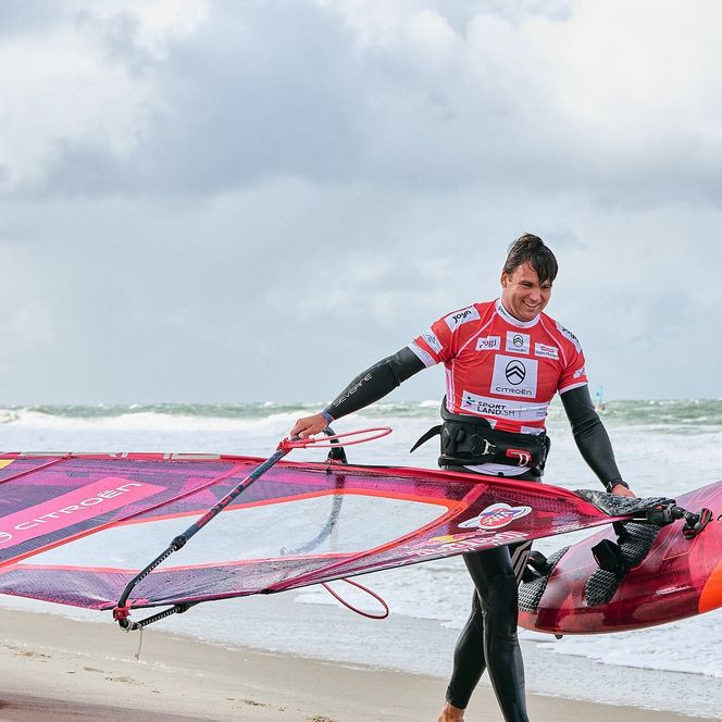 Windsurfer Philip Köster mit Board und Segel kommt lächelnd aus der Nordsee.