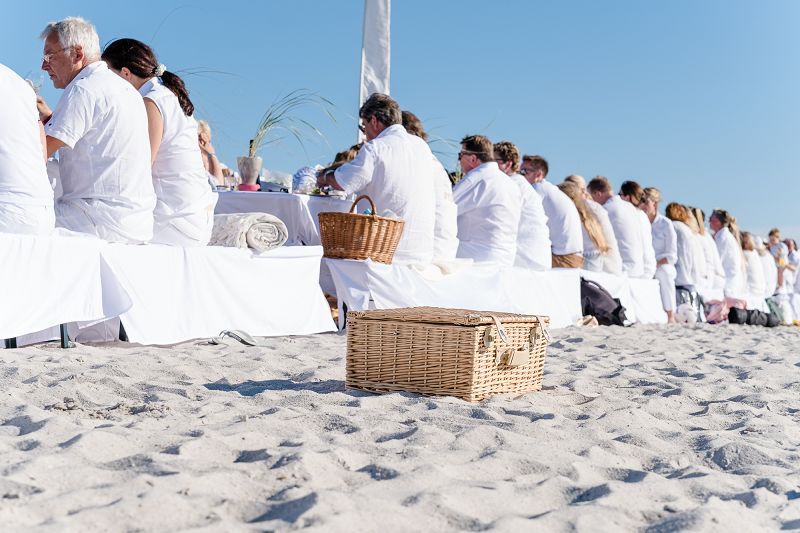 Menschen in Weiß sitzen am langen Tisch beim Strand-Dinner