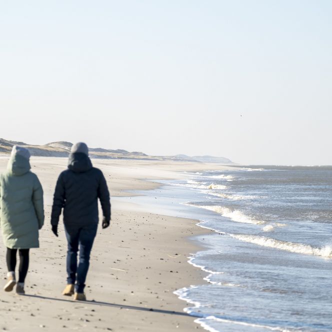 Zwei Personen gehen am leeren Winterstrand entlang.