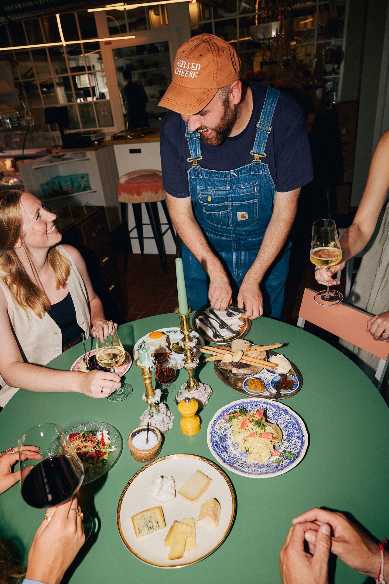 Lachende Menschen essen Käse und trinken Wein an grün gedecktem Tisch.