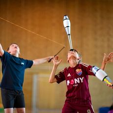 Zwei Jungen jonglieren in einer Sporthalle mit Diabolos; ein weiteres Diabolo ist im Vordergrund zu sehen.