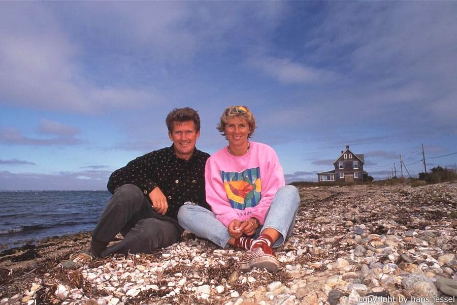 Zwei Menschen sitzen am Muschelstrand, Haus im Hintergrund.