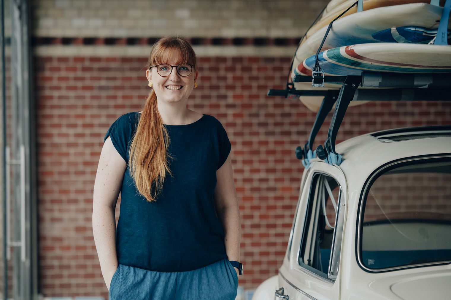 Lynn Scotti von Sylt Marketing steht lächelnd neben einem weißen Oldtimer mit Surfboards auf dem Dach.