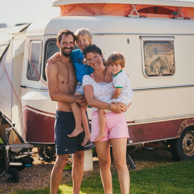 Eine Familie mit zwei Kindern posiert vor ihrem Wohnwagen in der Sonne. 