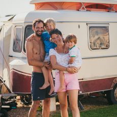 Eine Familie mit zwei Kindern posiert vor ihrem Wohnwagen in der Sonne.
