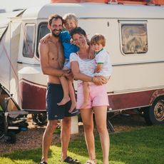 Eine Familie mit zwei Kindern posiert vor ihrem Wohnwagen in der Sonne.