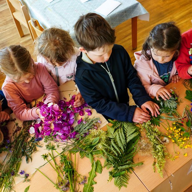 Kinder basteln an einem Tisch mit Blumen und Gräsern
