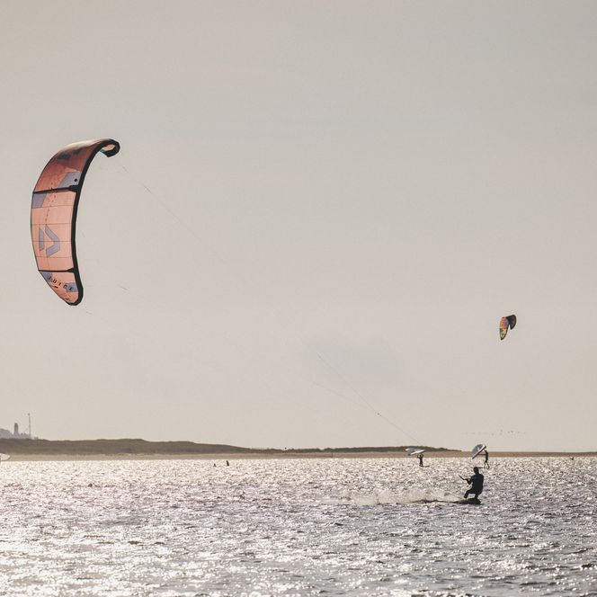 Kitesurfer gleiten auf dem Wasser, während der Kite hoch in der Luft schwebt.