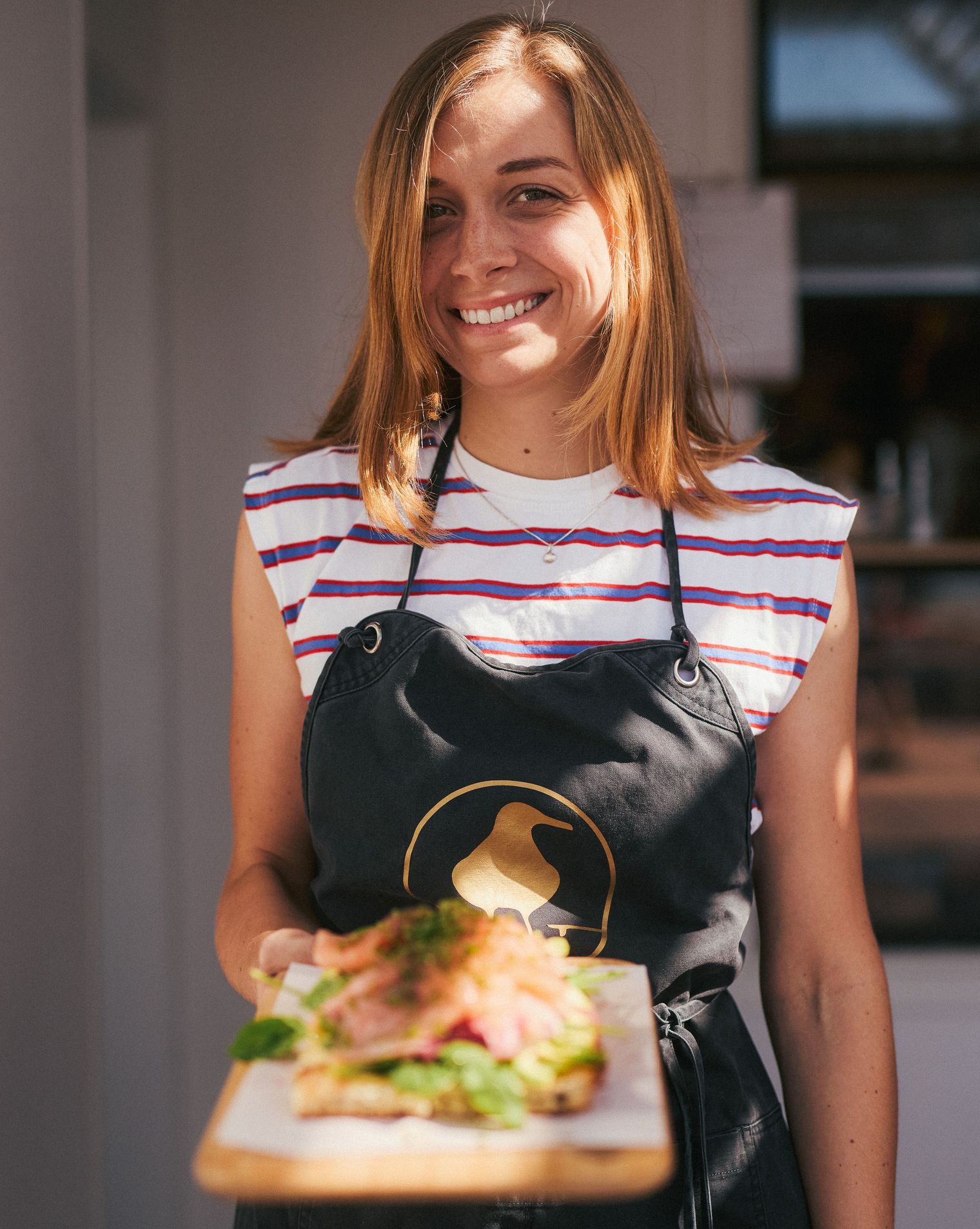 Woman presents a dish on a wooden board, wearing an apron with the “Zur Goldenen Möwe” logo.