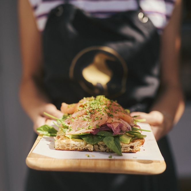 Sauerteigbrot mit Lachs, Spinat und Avocado auf einem Holzbrett präsentiert.