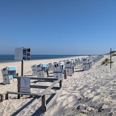 Strand mit weißen Strandkörben, Hinweisschildern und ruhiger Nordsee auf Sylt
