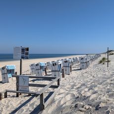 Strand mit weißen Strandkörben, Hinweisschildern und ruhiger Nordsee auf Sylt