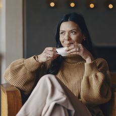 Frau sitzt entspannt mit Teetasse im gemütlichen Raum