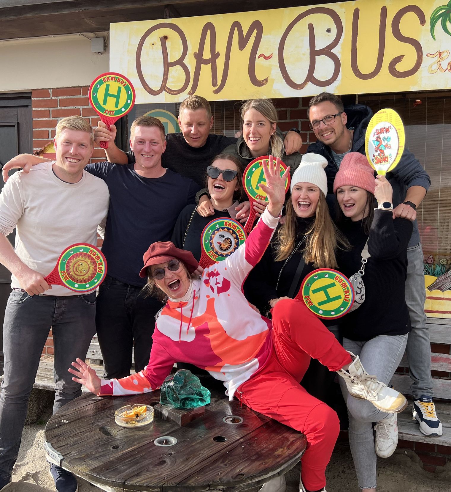Fröhliche Gruppe posiert lachend vor dem bunten „Bam Bus“-Imbiss.